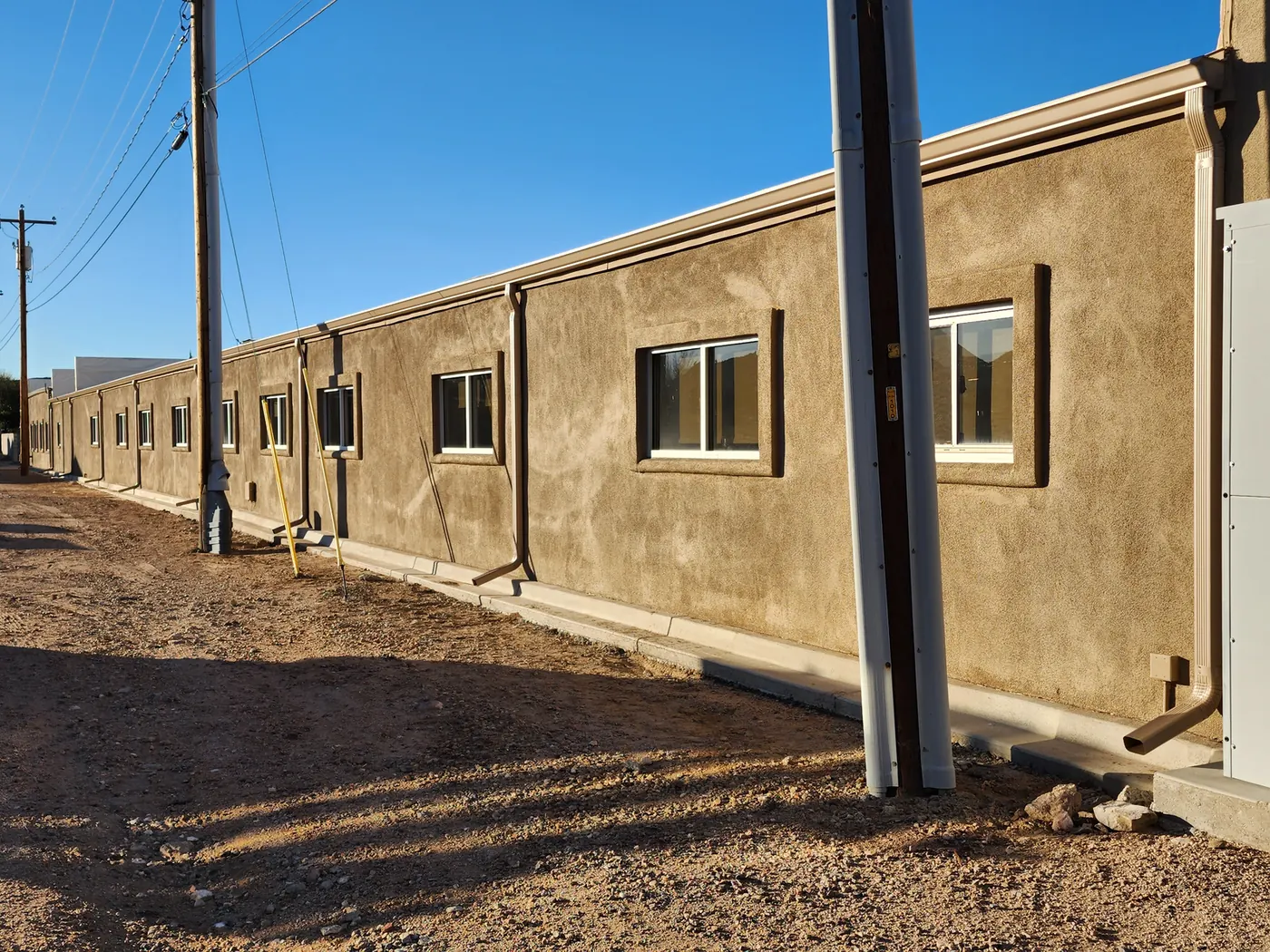 Tan seamless aluminum gutters and downspouts running along a long commercial stucco wall in Las Vegas, NV