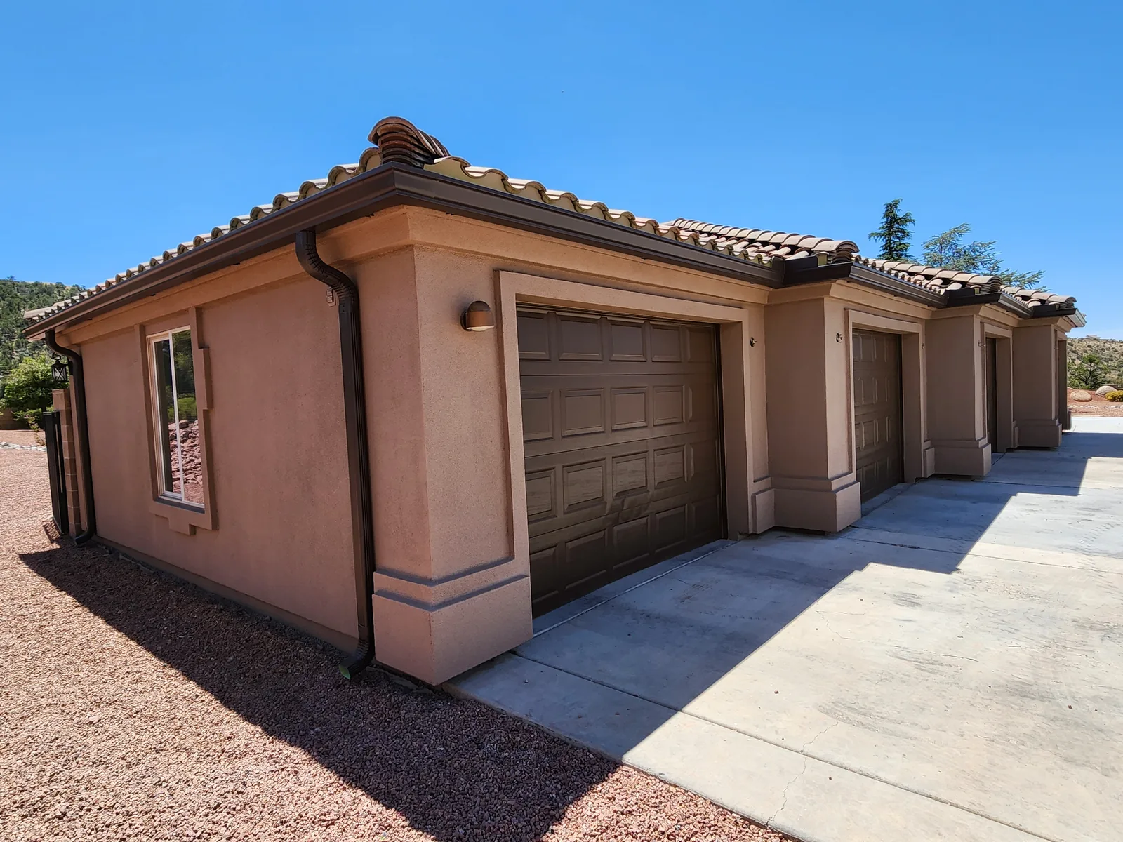 Dark brown seamless aluminum gutters and round downspouts on a clay-tile-roof stucco home in Kingman, AZ